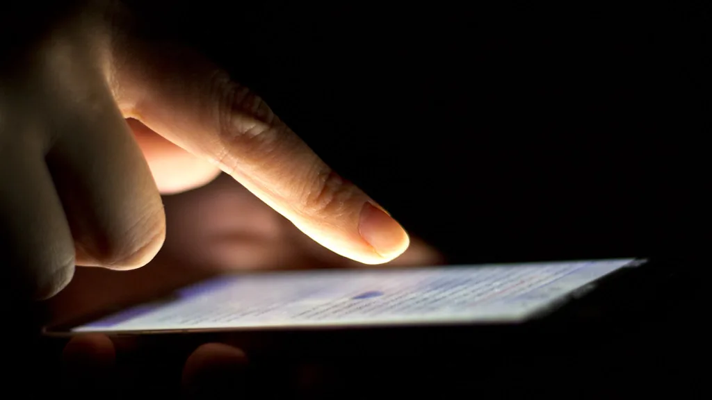 Persona usando un celular en la oscuridad, pantalla iluminada